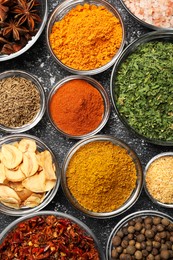 Glass bowls with different spices on grey textured table, flat lay