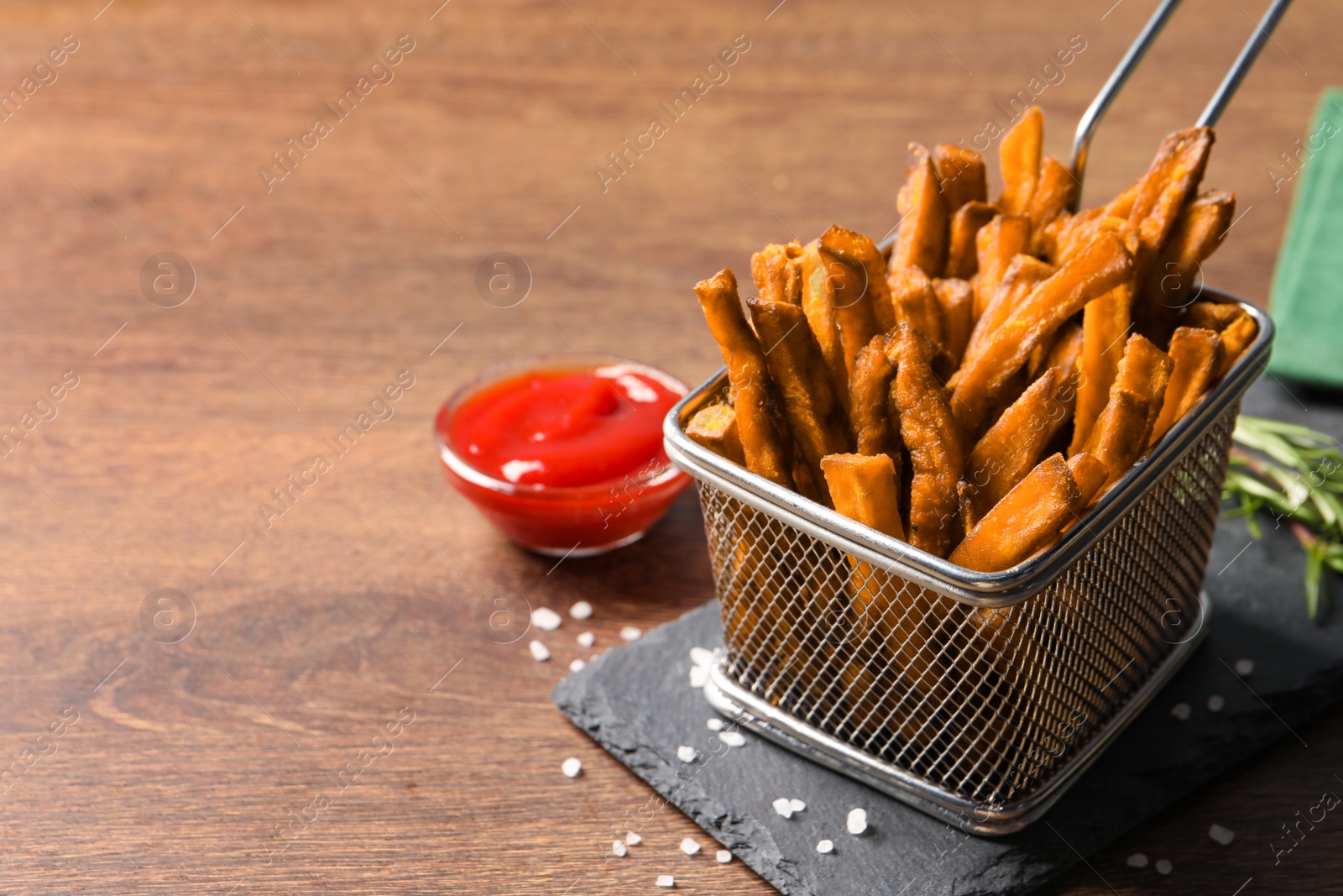 Photo of Frying basket with sweet potato fries and ketchup on wooden table, space for text