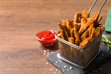 Photo of Frying basket with sweet potato fries and ketchup on wooden table, space for text