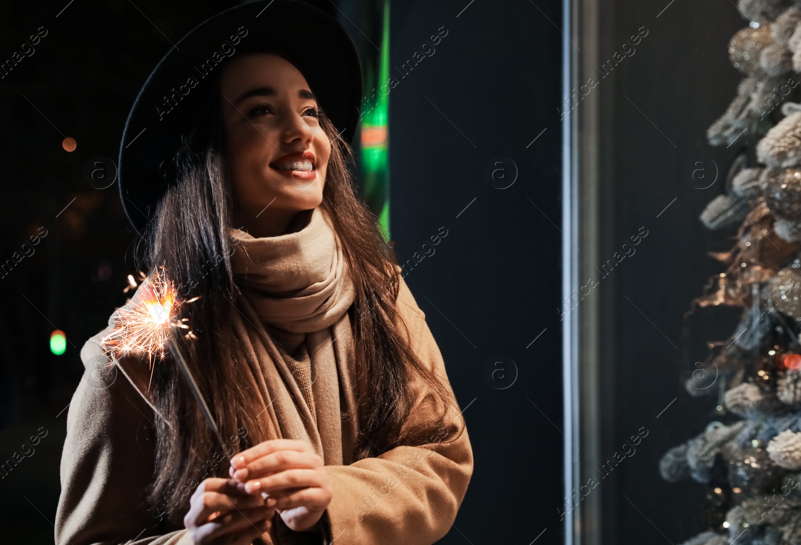 Photo of Woman in warm clothes holding burning sparkler outdoors