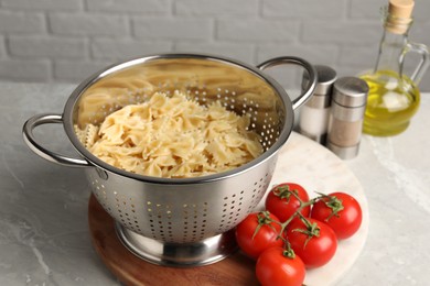 Cooked pasta in metal colander and tomatoes on grey marble table, closeup