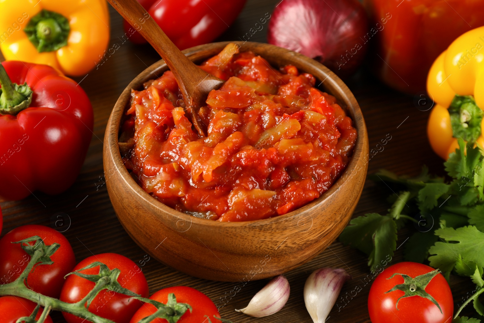 Photo of Tasty lecho in wooden bowl and fresh ingredients on table, closeup