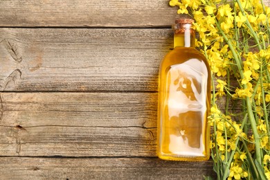 Photo of Rapeseed oil in glass bottle and beautiful yellow flowers on wooden table, flat lay. Space for text