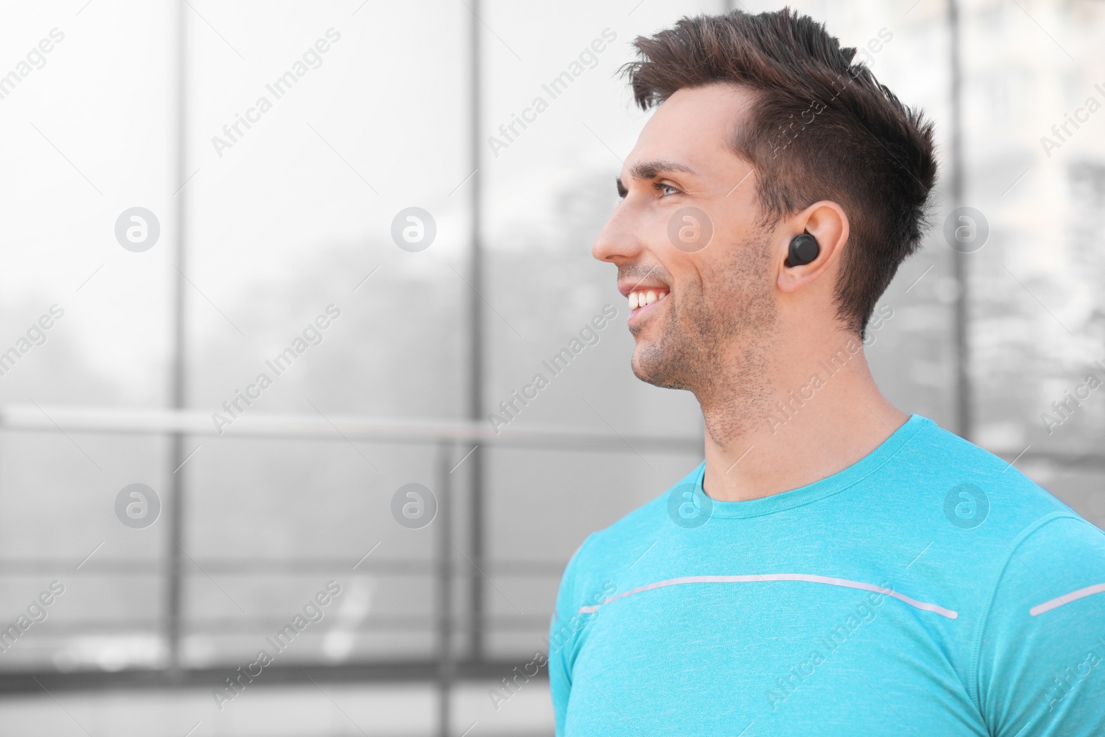 Photo of Young sportsman with wireless earphones on city street