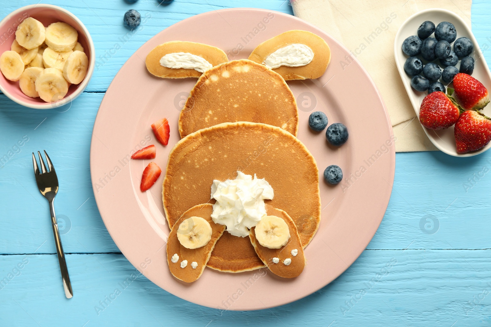 Photo of Creative serving for kids. Plate with cute bunny made of pancakes, berries, cream and banana on light blue wooden table, flat lay