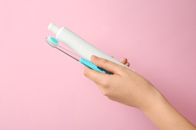 Woman holding toothbrush and paste against color background. Dental care