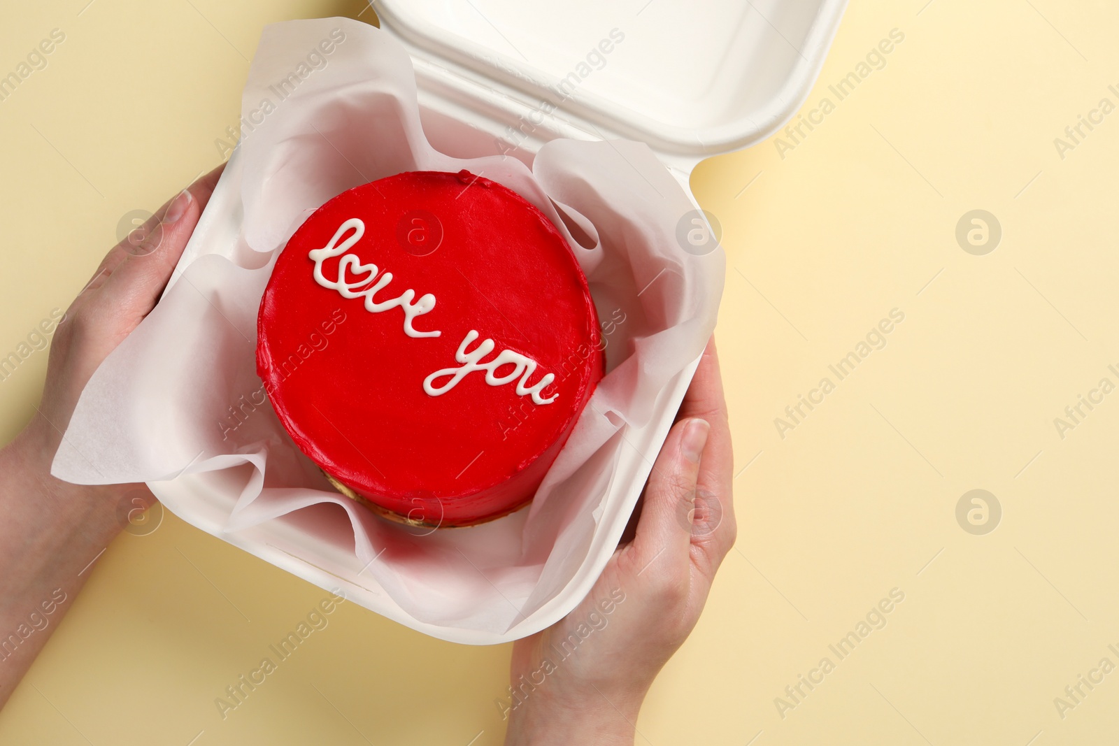 Photo of Woman holding takeaway box with bento cake at beige table, top view. St. Valentine's day surprise