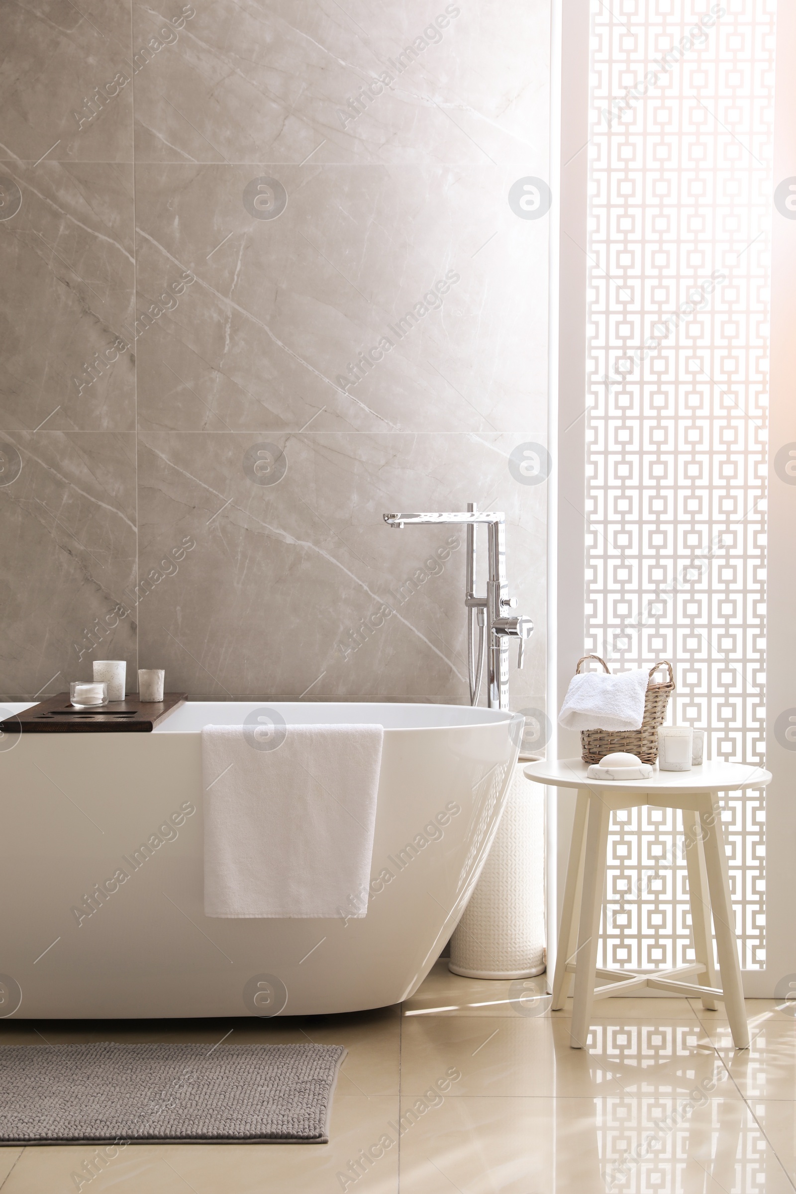 Photo of Modern white tub and table with toiletries in bathroom. Interior design