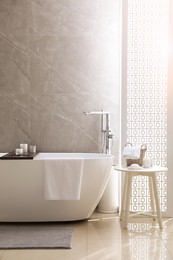 Photo of Modern white tub and table with toiletries in bathroom. Interior design