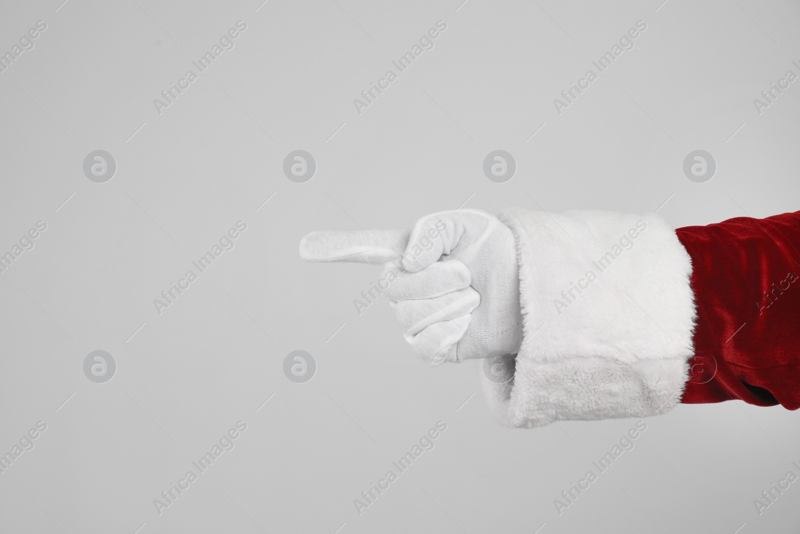 Photo of Santa Claus pointing at something on light grey background, closeup of hand