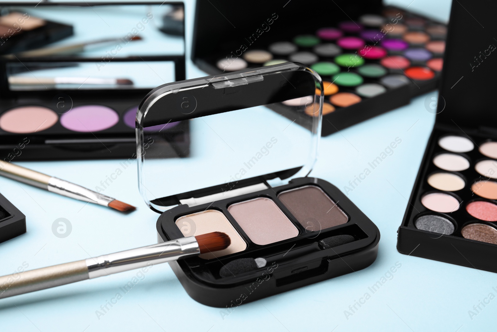 Photo of Beautiful eye shadow palettes and brushes on light blue background