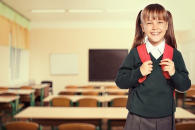 Little girl with backpack in empty school classroom