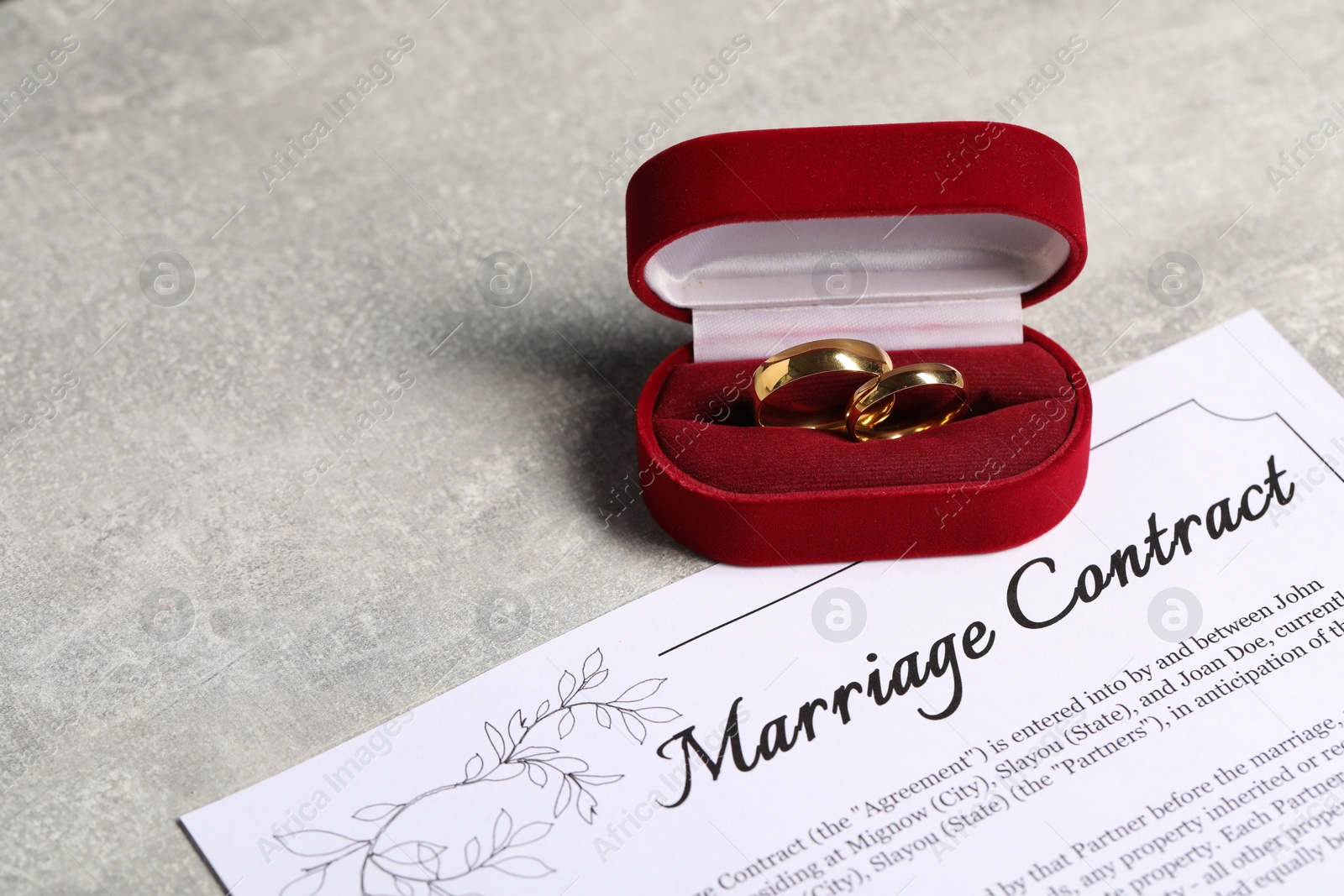 Photo of Marriage contract and golden wedding rings on grey table, space for text