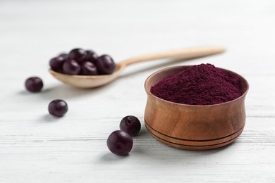 Bowl with acai powder and fresh berries on light wooden table