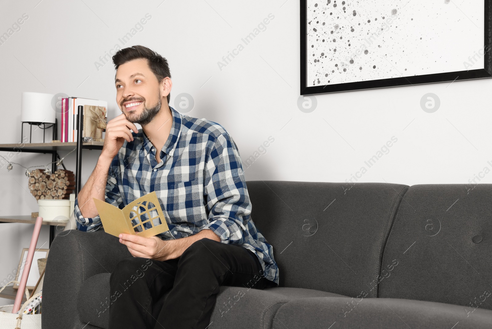 Photo of Happy man holding greeting card on sofa in living room