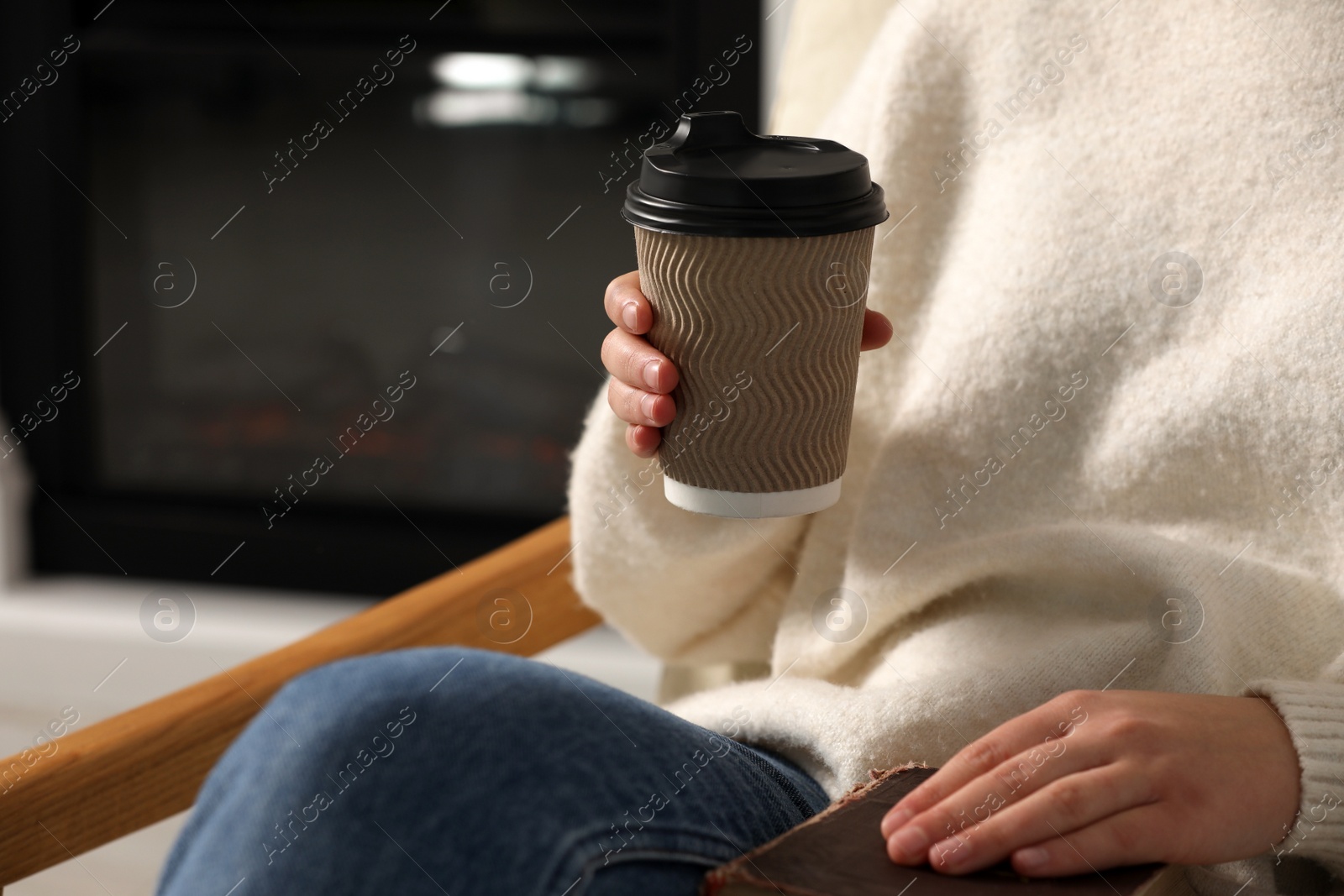 Photo of Woman holding takeaway cardboard cup and book indoors, closeup. Coffee to go