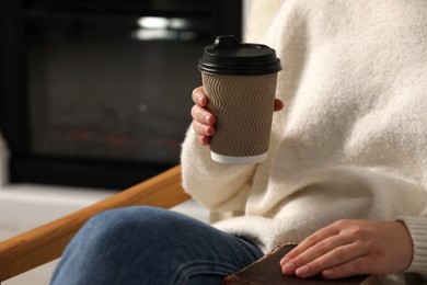 Photo of Woman holding takeaway cardboard cup and book indoors, closeup. Coffee to go