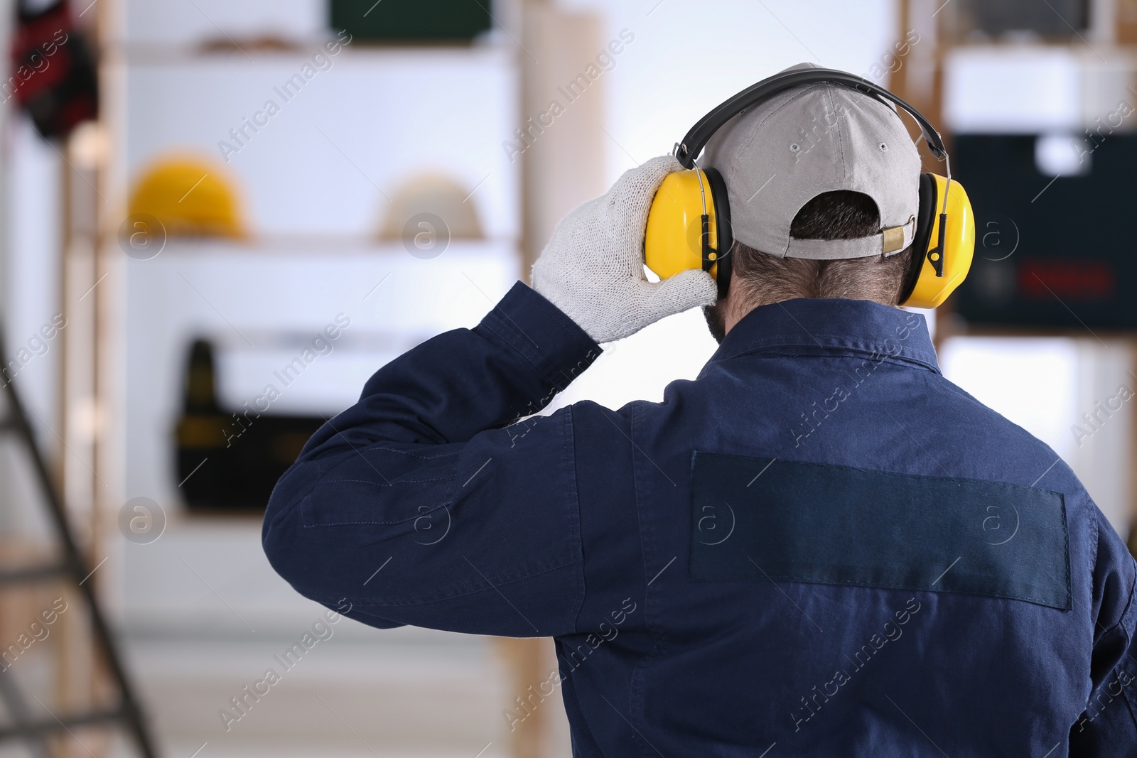 Photo of Worker wearing safety headphones indoors, back view. Hearing protection device