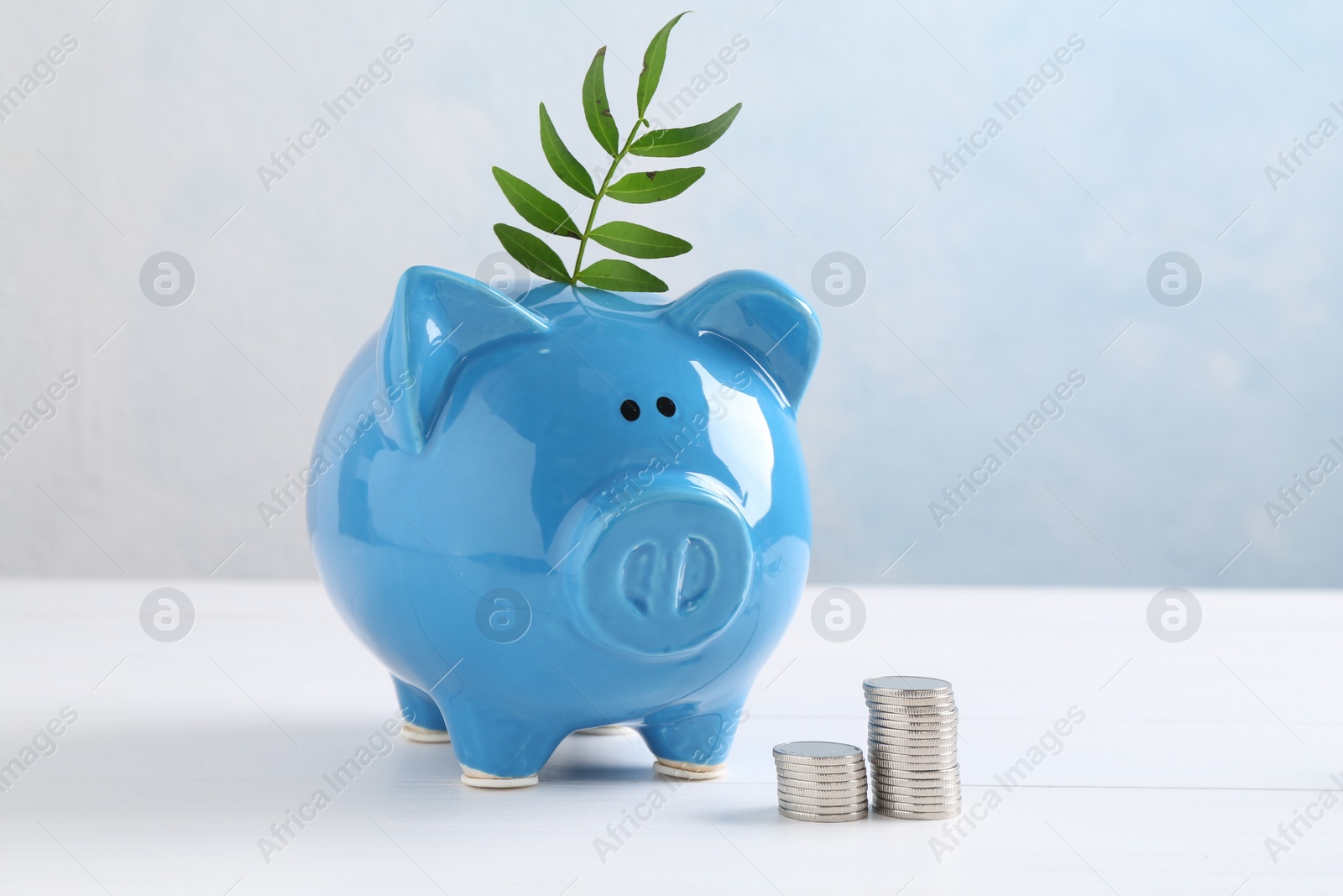 Photo of Financial savings. Piggy bank with green twig and stacked coins on white table