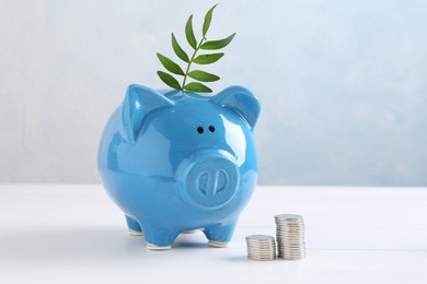 Photo of Financial savings. Piggy bank with green twig and stacked coins on white table