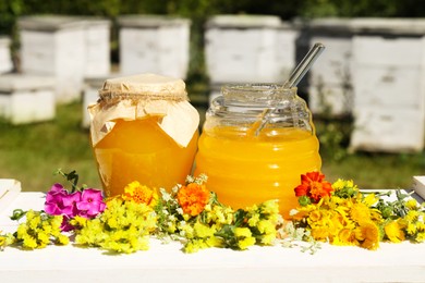 Photo of Delicious fresh honey and beautiful flowers on white wooden table in apiary