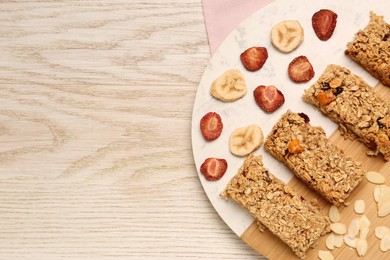 Tasty granola bars, dried strawberries, bananas and almond flakes on wooden table, top view. Space for text