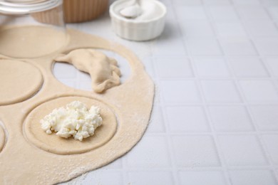 Photo of Process of making dumplings (varenyky) with cottage cheese. Raw dough and ingredients on white tiled table, closeup. Space for text