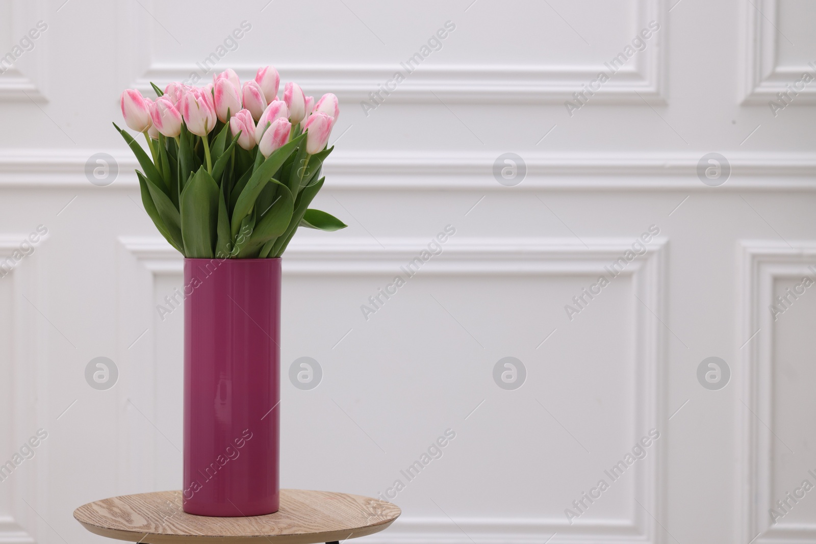 Photo of Beautiful bouquet of fresh pink tulips on table near white wall. Space for text