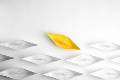 Photo of Yellow paper boat floating away from others on white background, flat lay. Uniqueness concept