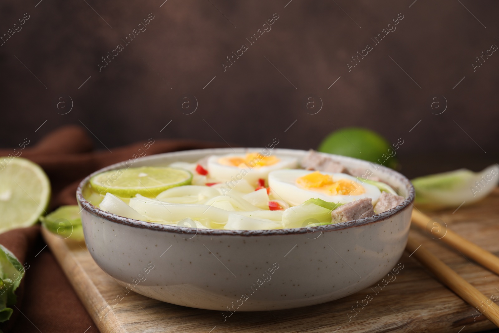 Photo of Bowl of delicious rice noodle soup with meat and egg on wooden board, closeup