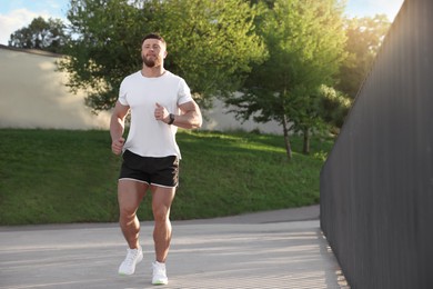 Photo of Young man running outdoors on sunny day. Space for text