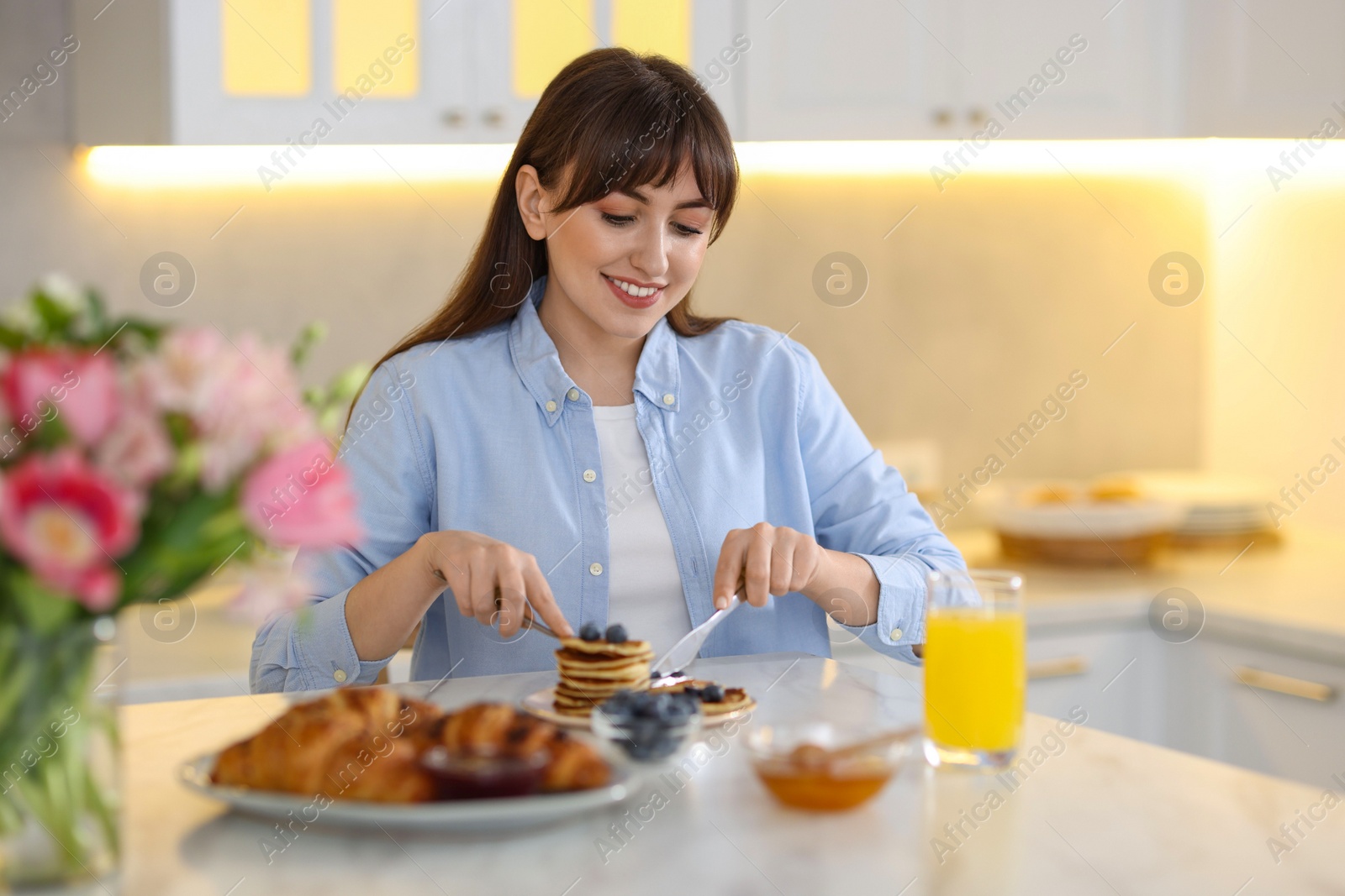 Photo of Smiling woman eating tasty pancakes at breakfast indoors