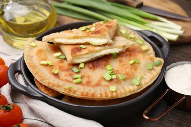 Photo of Delicious fried chebureki with cheese and green onion on wooden table