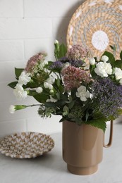 Ceramic vase with beautiful bouquet on light table near white brick wall