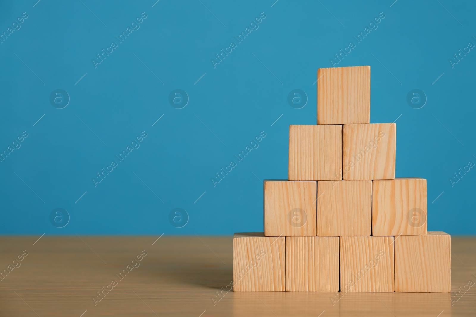 Photo of Pyramid of blank cubes on wooden table against light blue background. Space for text