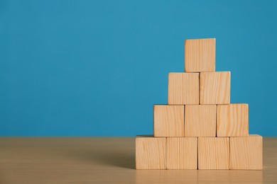 Photo of Pyramid of blank cubes on wooden table against light blue background. Space for text