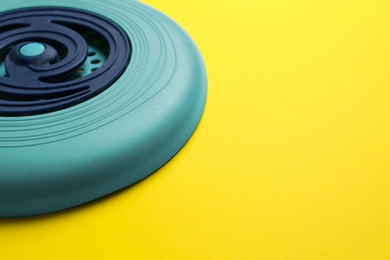 Blue plastic frisbee disk on yellow background, closeup. Space for text