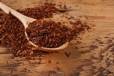 Photo of Spoon with dry rooibos leaves on wooden table, closeup. Space for text