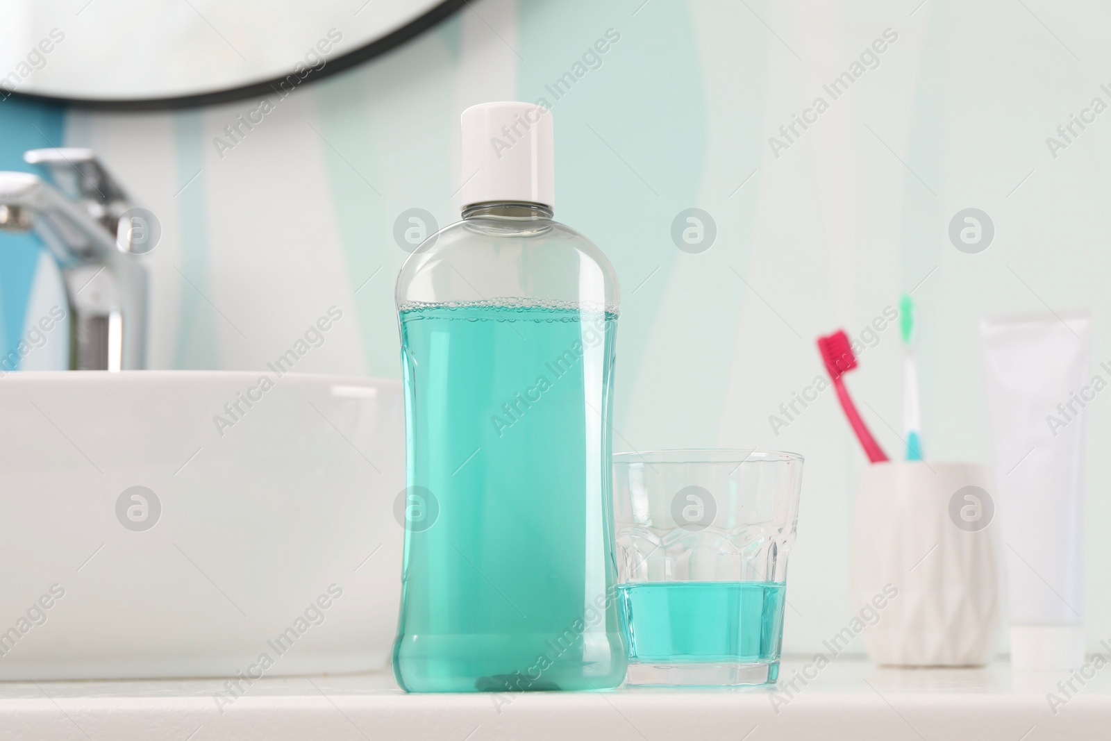 Photo of Bottle of mouthwash, toothbrushes and glass on white table in bathroom