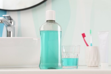 Bottle of mouthwash, toothbrushes and glass on white table in bathroom