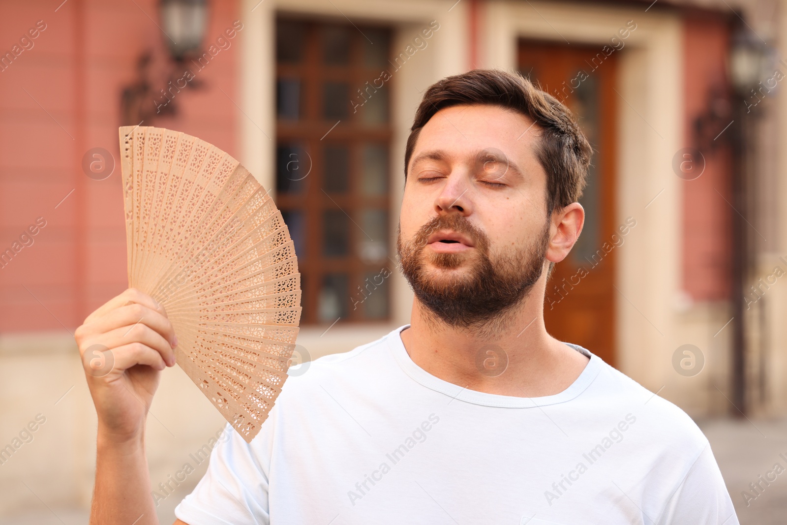 Photo of Man with hand fan suffering from heat outdoors