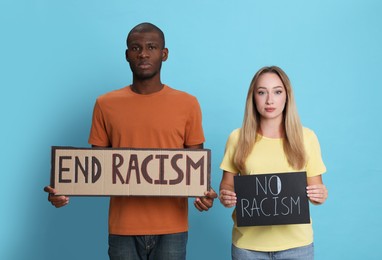 Young woman and African American man holding signs with phrase End Racism on light blue background