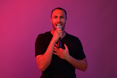 Photo of Handsome man with microphone singing on pink background. Color tone effect