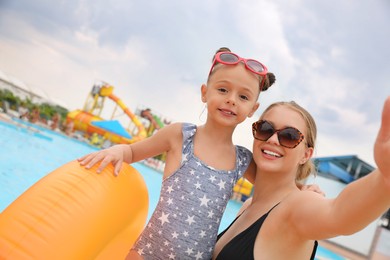Photo of Mother and daughter taking selfie near pool in water park. Family vacation