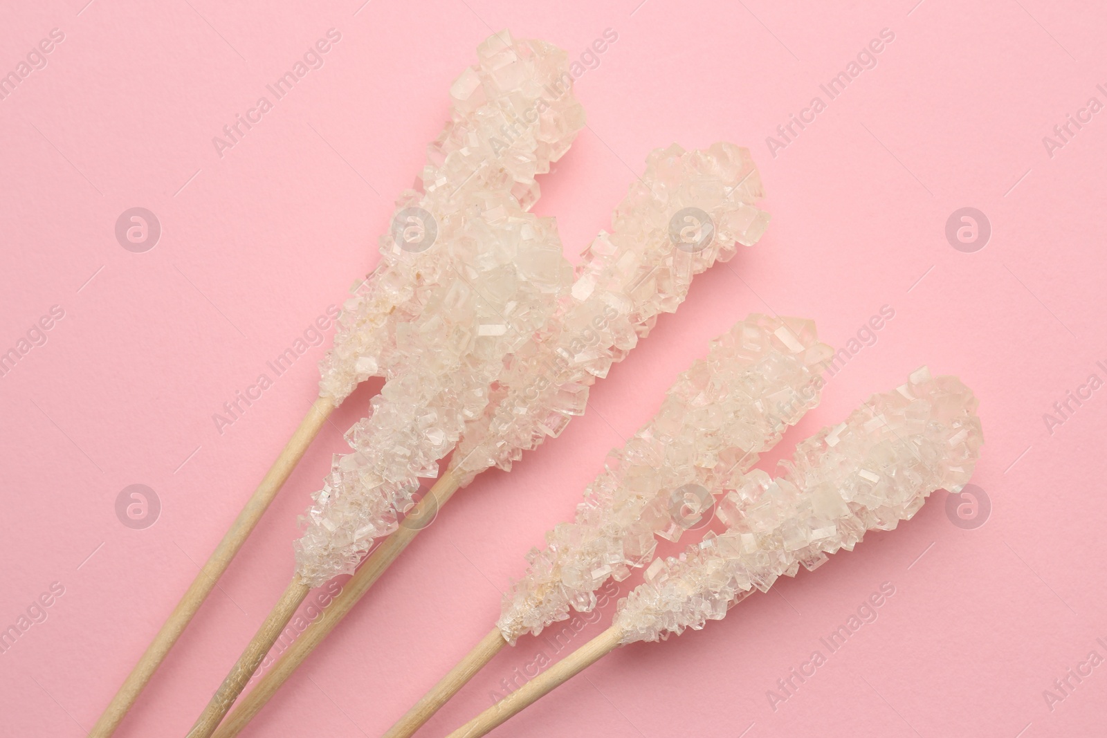 Photo of Wooden sticks with sugar crystals on pink background, flat lay. Tasty rock candies