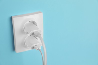 Photo of Charger adapters plugged into power sockets on light blue wall, space for text. Electrical supply