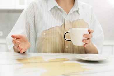 Photo of Woman with spilled coffee over her shirt at marble table in kitchen, closeup