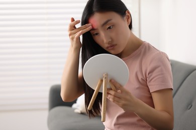 Suffering from allergy. Young woman with mirror checking her face in living room