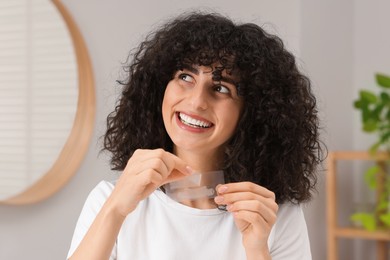 Photo of Young woman holding teeth whitening strips indoors