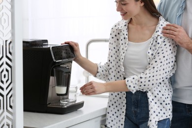 Photo of Happy couple preparing fresh aromatic coffee with modern machine in kitchen, closeup